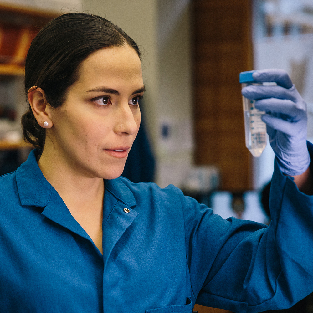 Markita del Carpio Landry wearing a blue lab holding up a vial.