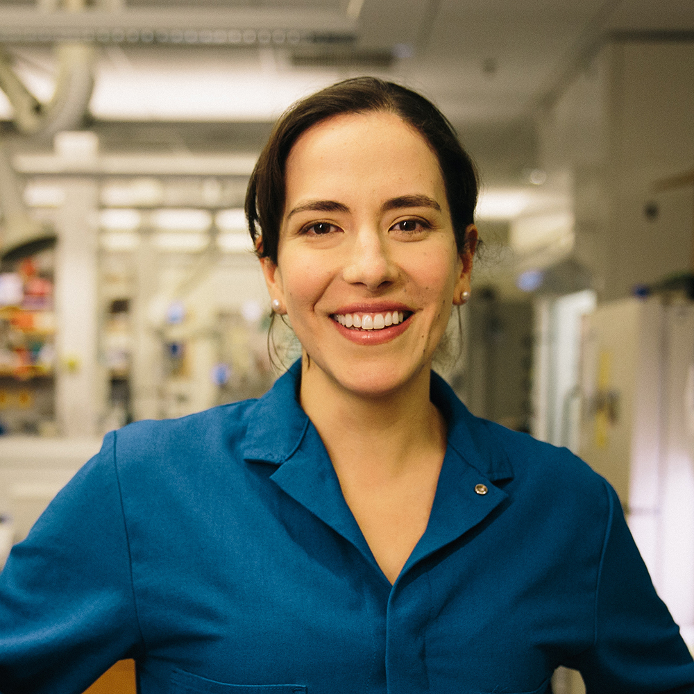 Markita del Carpio Landry wearing a blue lab coat smiling in her lab.