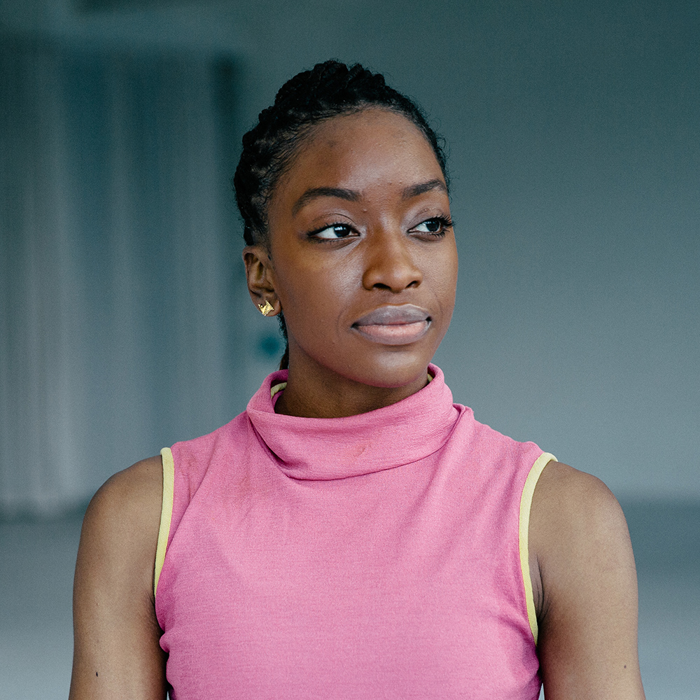 Tamisha Guy, in a pink shirt, stands in a large loft studio.
